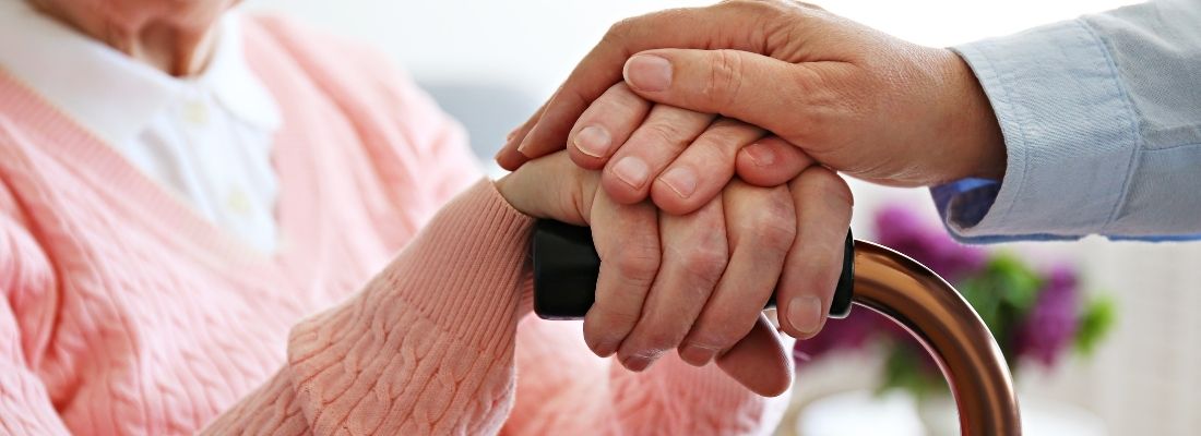 Eine Hand liegt auf der Hand einer älteren Person am Gehstock